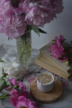 A cozy still life of pink flowers, a coffee cup, and books for a tranquil setting.