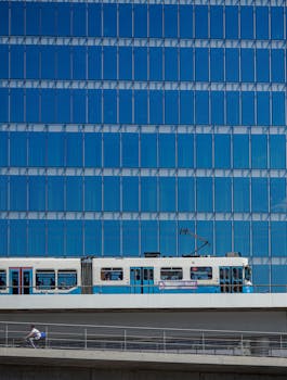 Blue tram passing by a reflective skyscraper, showcasing urban architecture and transportation.