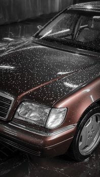 Close-up of a brown car covered in water droplets at a car wash, showcasing luxury vehicle details.