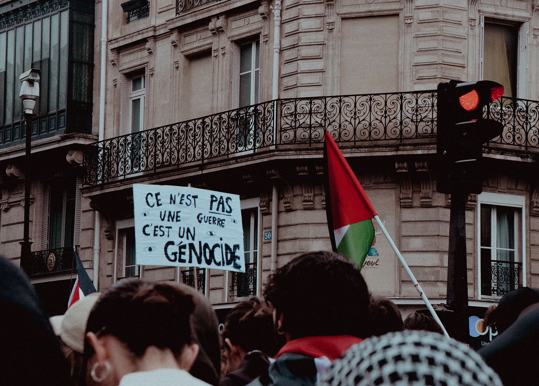 Protesters gather in Paris with flags and a sign against genocide, highlighting civil unrest.