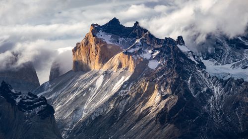 Free Stunning view of Torres del Paine mountains basking in the soft light of sunrise with clouds enveloping the peaks. Stock Photo
