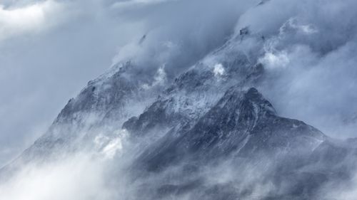 Free A breathtaking view of snow-covered mountain peaks enveloped in misty clouds, showcasing nature's grandeur. Stock Photo