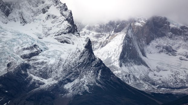 Majestic snow-capped mountains with dramatic rock formations and foggy atmosphere.