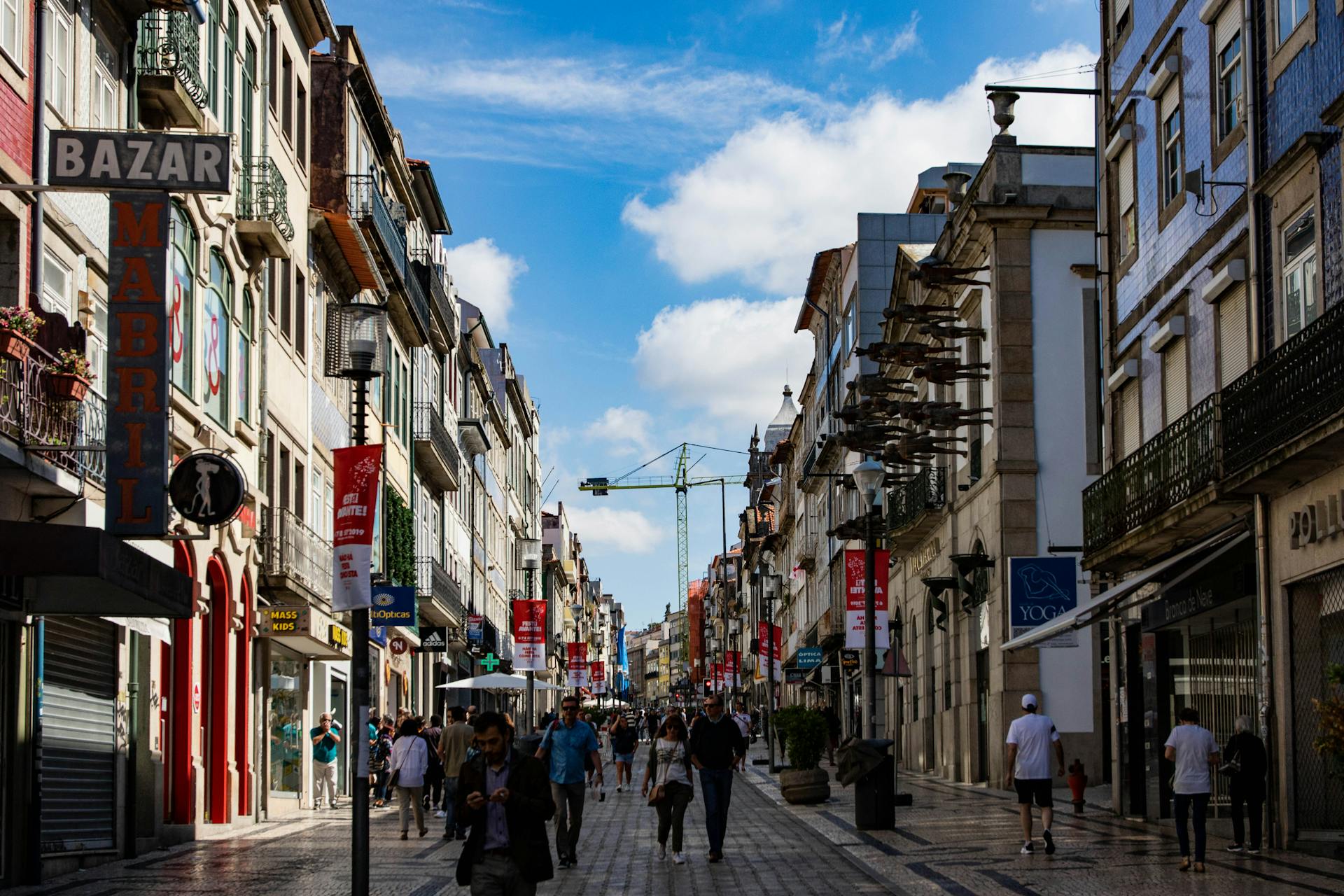 Lively street scene in Porto, Portugal with shops and pedestrians under a bright blue sky.