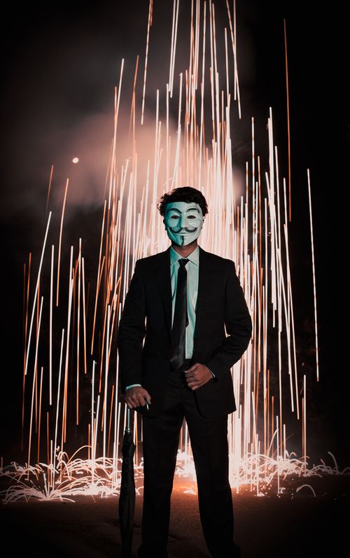 Free Man in a suit wearing a mask stands against a backdrop of fireworks in Jaipur at night. Stock Photo