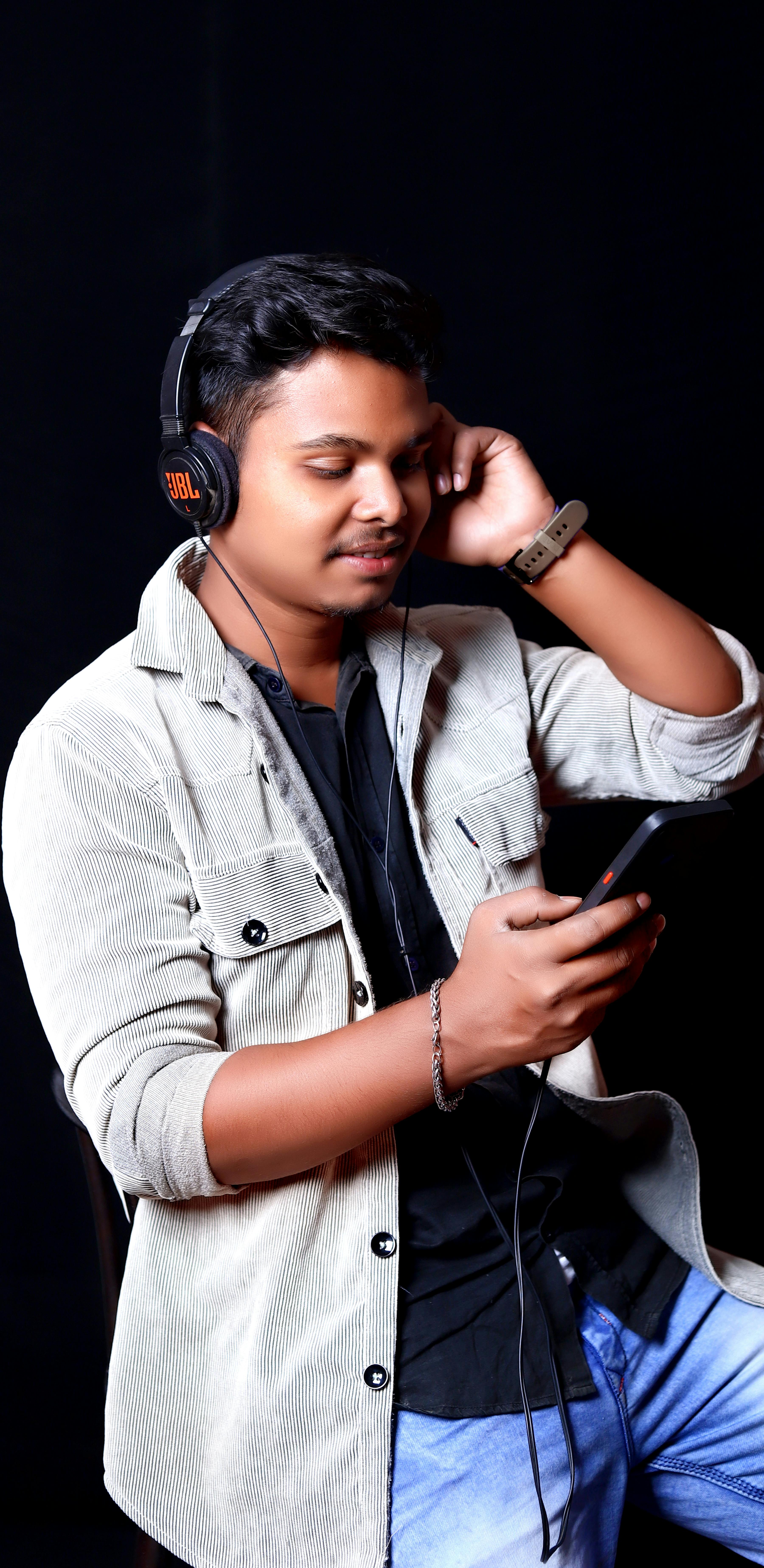 A young man wearing headphones, engaged with his smartphone against a black background.