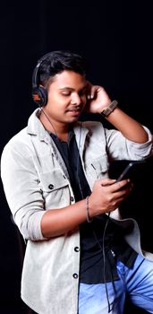 A young man wearing headphones, engaged with his smartphone against a black background.
