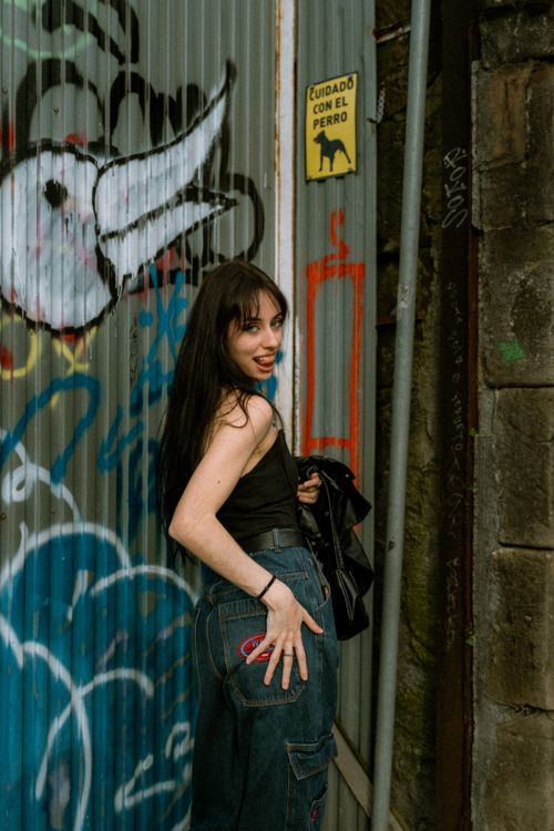 Free A young woman poses cheerfully next to colorful graffiti on an urban street. Stock Photo