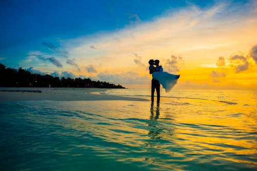 Man carrying a woman on seashore during golden hour