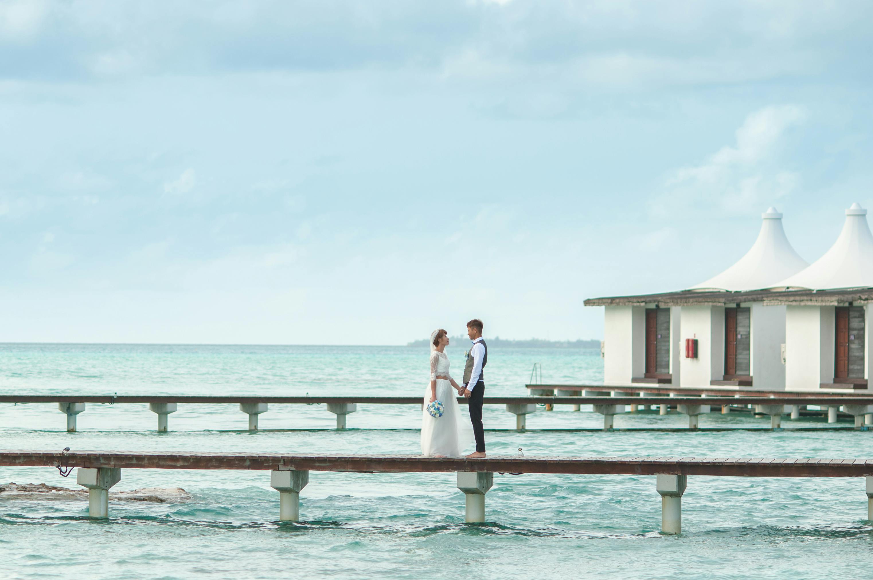 Bride and groom hold hands on an ocean jetty, with stunning sea views in a serene setting.