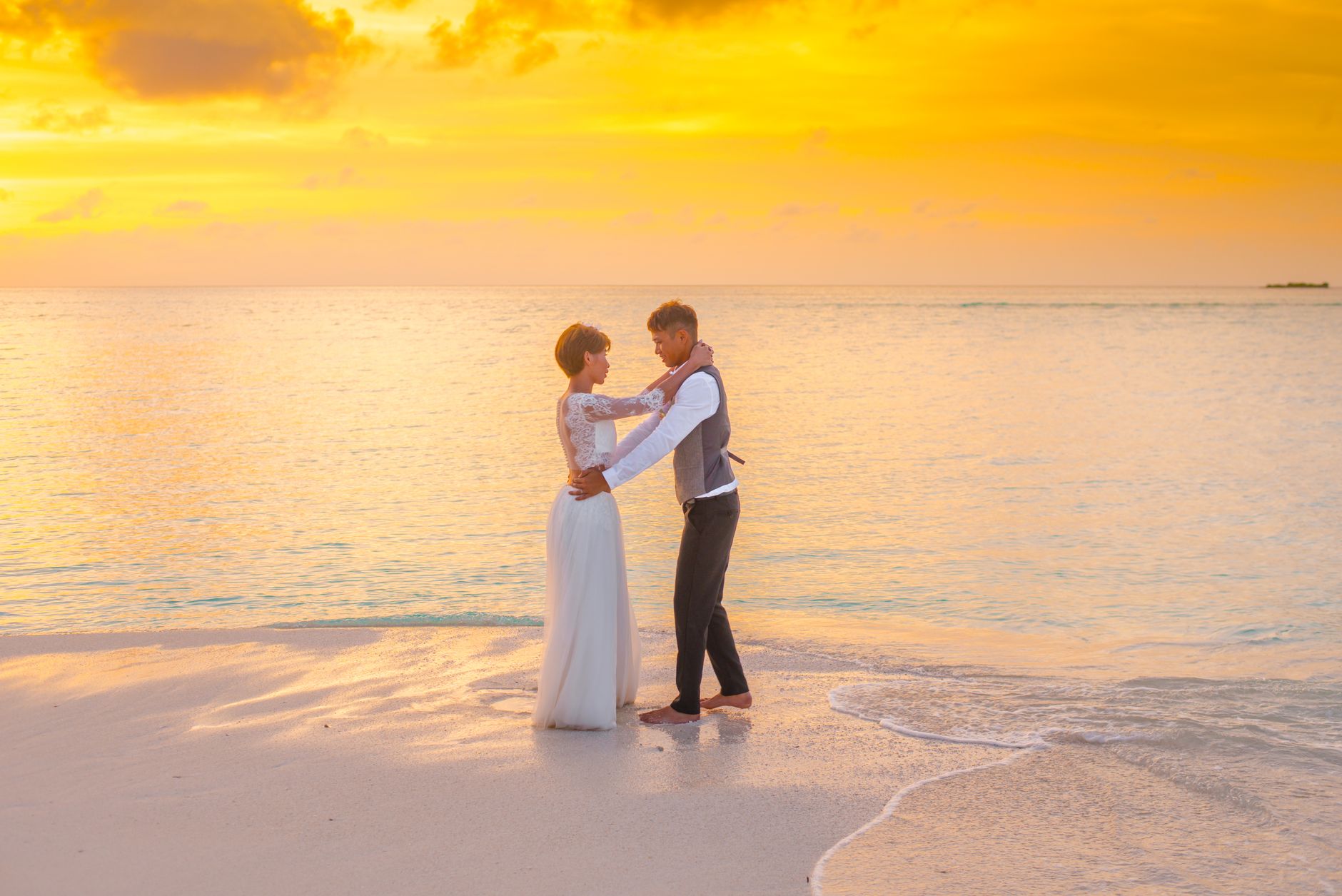 Couple in wedding attire embracing on a golden beach at sunset