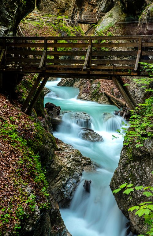 Free A tranquil shot of a waterfall cascading under a wooden bridge, set in the lush greenery of Tirol, Austria. Stock Photo