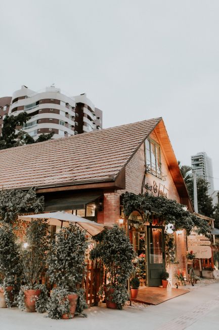 Cozy brick restaurant facade with potted trees, urban backdrop, evening ambiance.