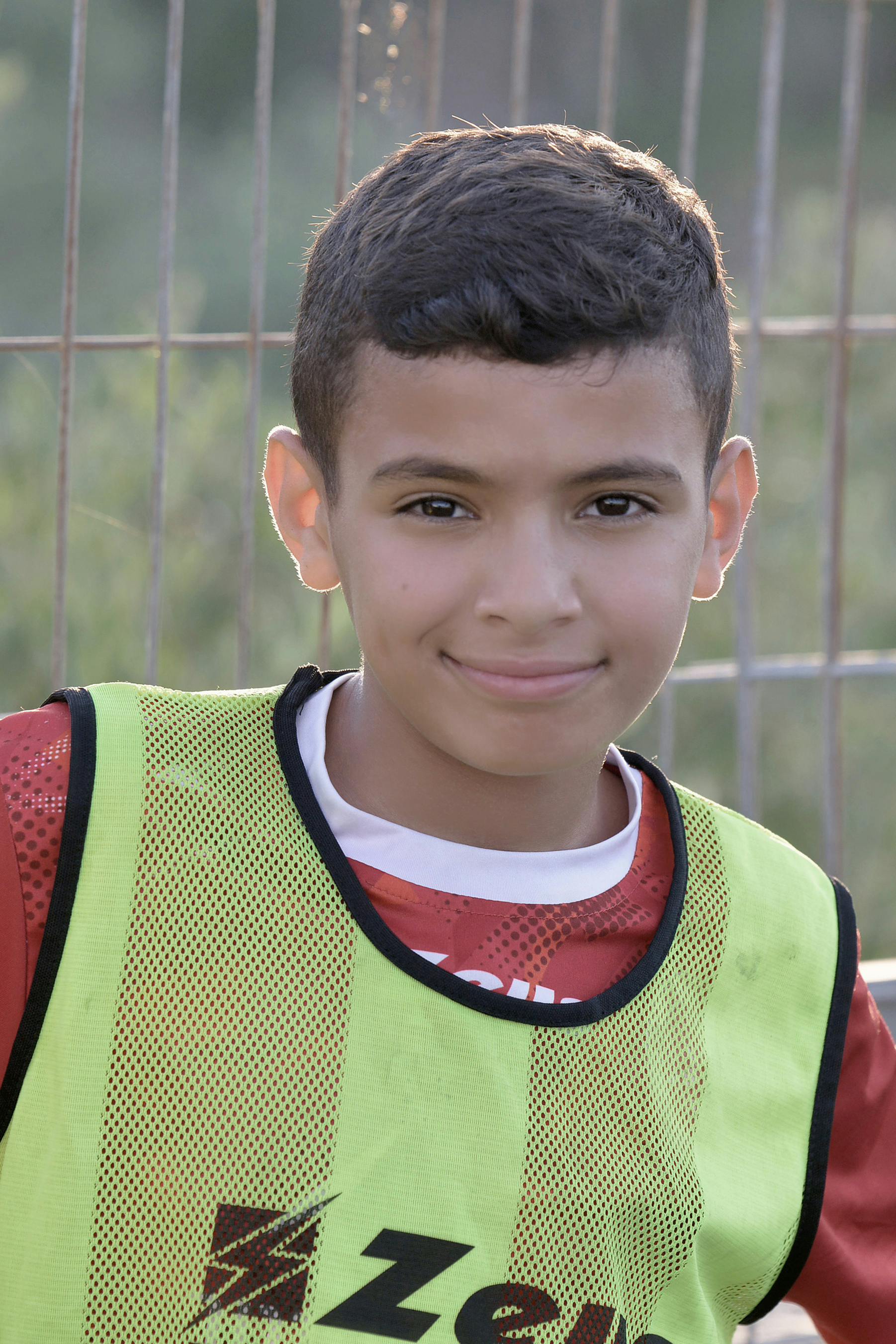A cheerful young boy in sportswear smiling at the camera outdoors on a sunny day.