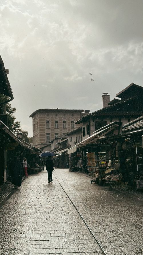 Free A serene rainy day in a city street market with pedestrians and stalls. Stock Photo