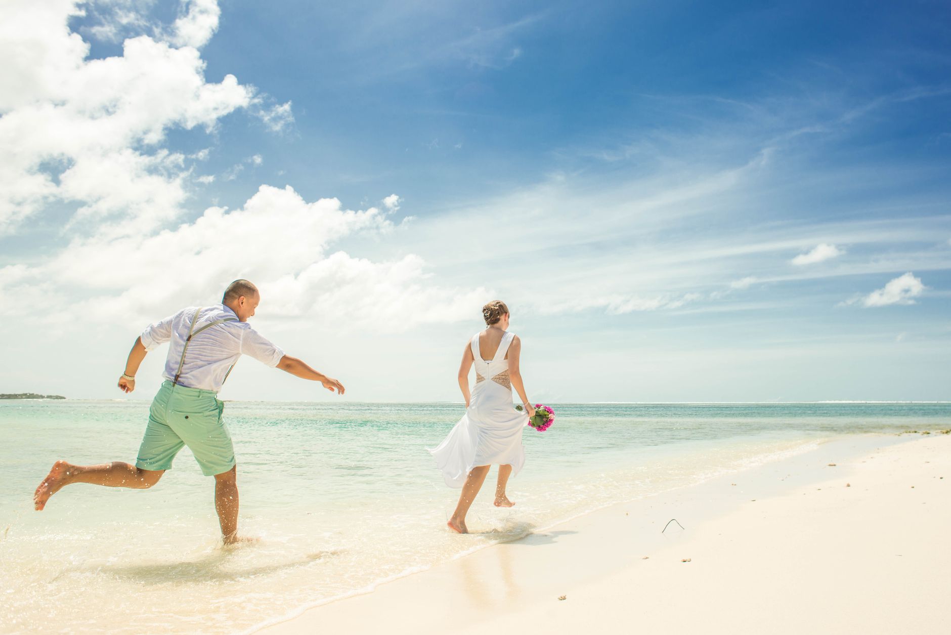 folkloric dancers for weddings egypt — A couple in wedding attire joyfully running along a sunny tropical beach.