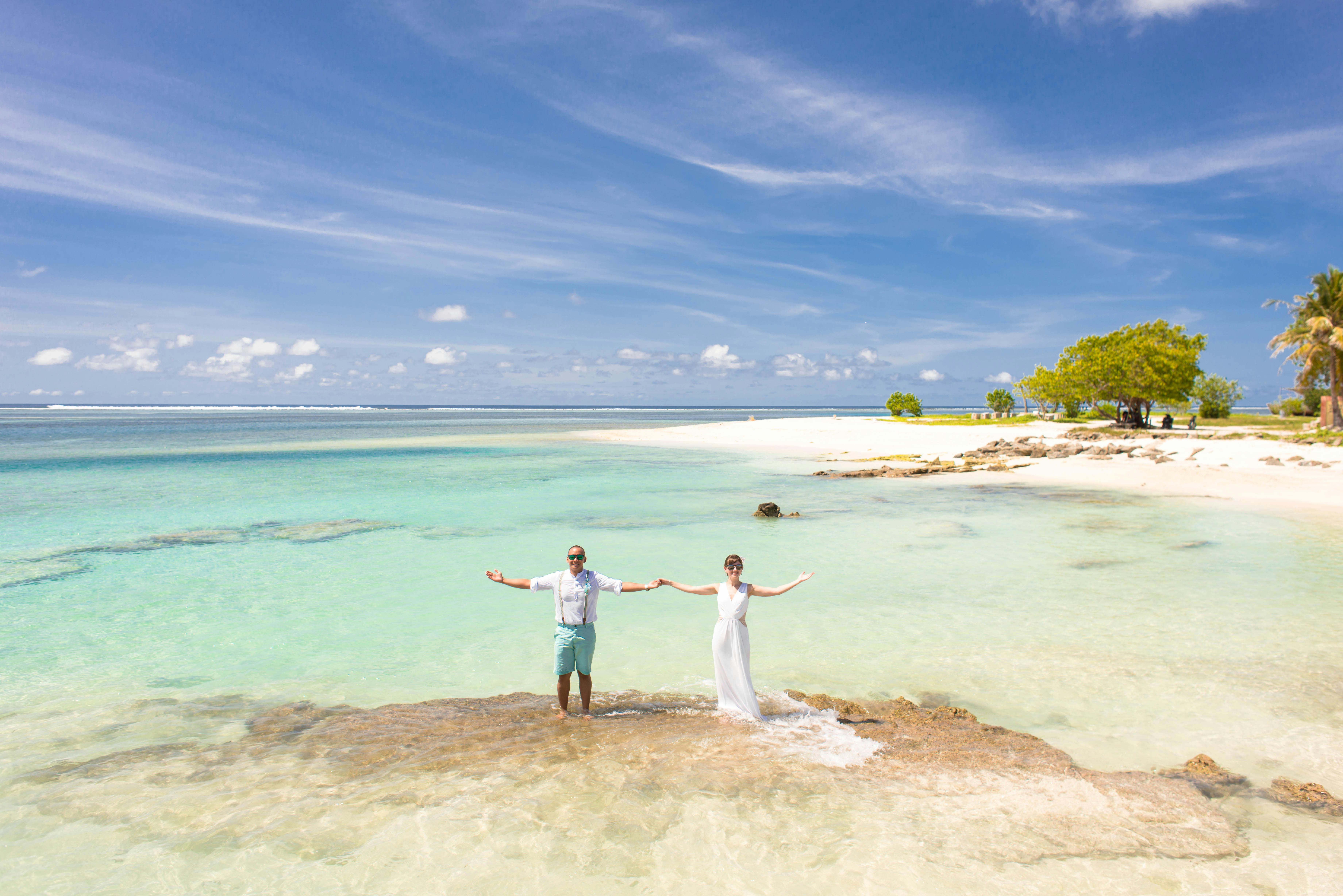 A couple poses joyfully on a stunning tropical beach under a clear blue sky.