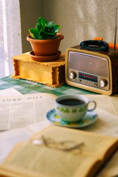 A still life scene with a vintage radio, coffee cup, books, and a potted plant, exuding warmth and nostalgia.