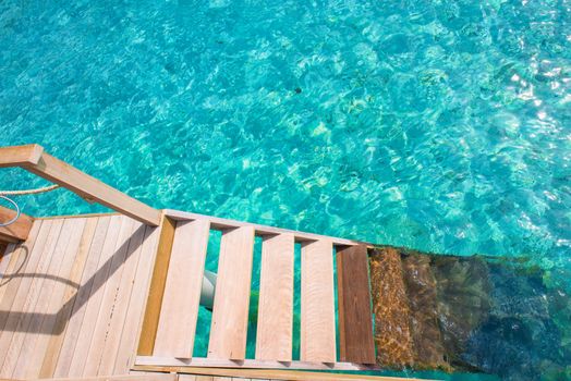 View of wooden stairs leading into clear, turquoise tropical sea water, perfect for vacation inspiration.