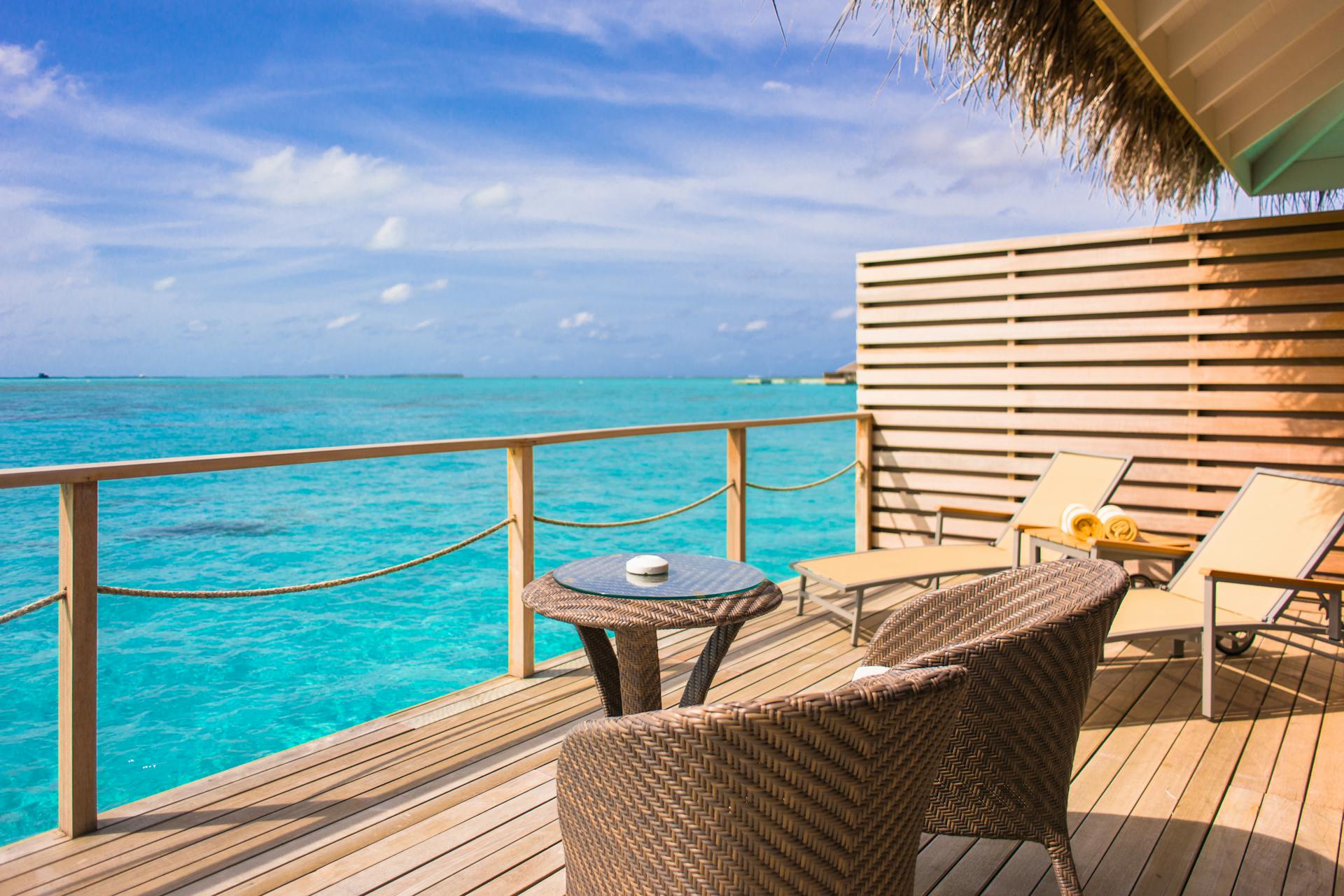 Relaxing oceanfront deck with wicker chairs and table, overlooking turquoise waters under blue skies.