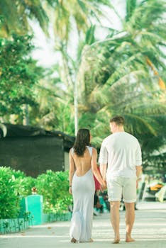 A couple leisurely strolls hand in hand on a lush tropical path, showcasing romance and tranquility.