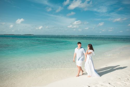 Free Couple walking hand in hand on a tropical beach, enjoying a romantic moment under a bright sky. Stock Photo