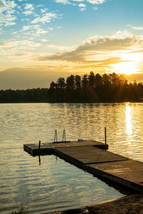 Free Peaceful lake scene at sunset with a wooden pier and trees in the background. Stock Photo