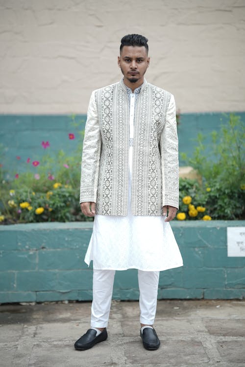 A man in white and gold sherwani standing outside