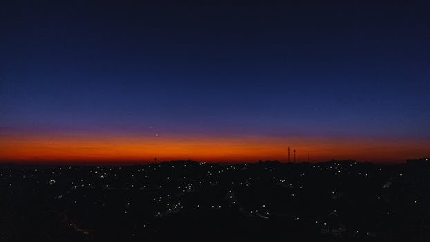 城市景观之上，令人惊叹的日落创造出戏剧性的天际线，下方灯光闪烁