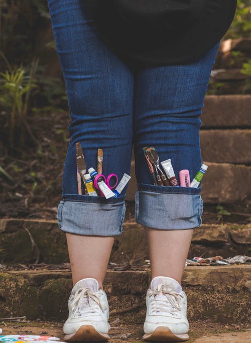 A person with jeans and shoes with pens and pencils