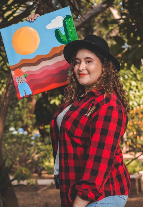 A woman holding up a painting of a desert scene