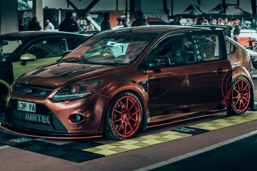 A sleek brown Ford sports car with custom tuning displayed at an automotive event.