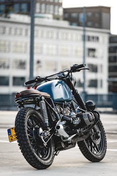 一辆时尚的咖啡馆赛车摩托车停放在柏油路上，背景是现代建筑