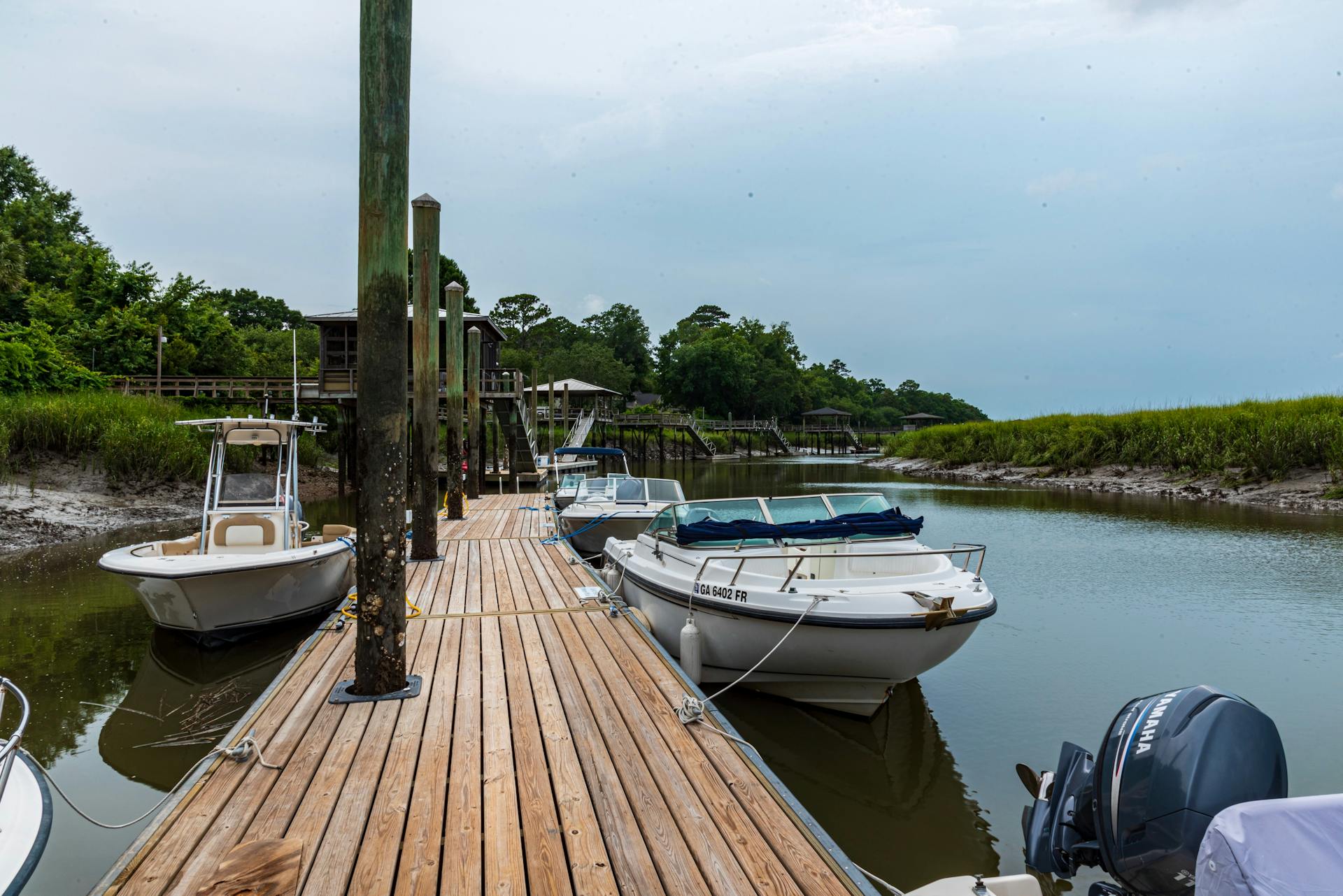 Peaceful scene of boats docked at a wooden pier in a lush, green harbor during summer.