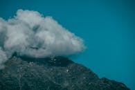 在明亮的蓝天下，崎岖的岩石山峰半掩于云层之中，景象令人惊叹