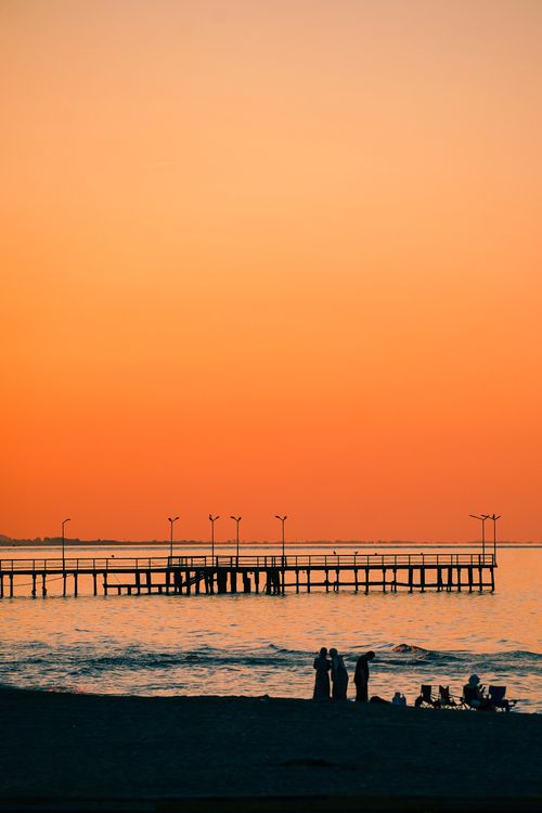 Free Silhouetted people enjoy the warm sunset by a pier in Samsun, Türkiye. Relaxing coastal scene. Stock Photo