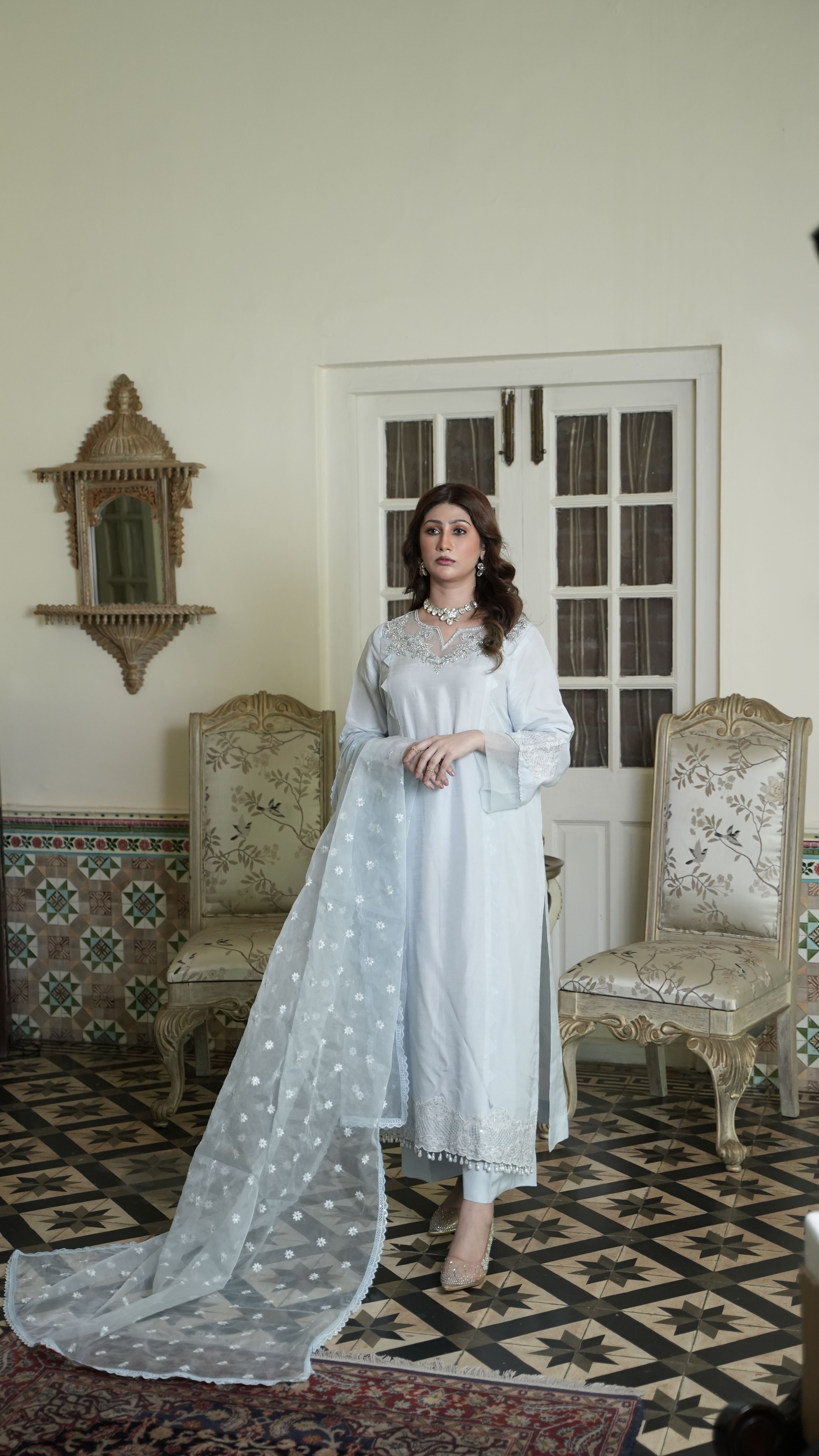 Woman in a stylish tunic and scarf poses elegantly indoors against a vintage backdrop.