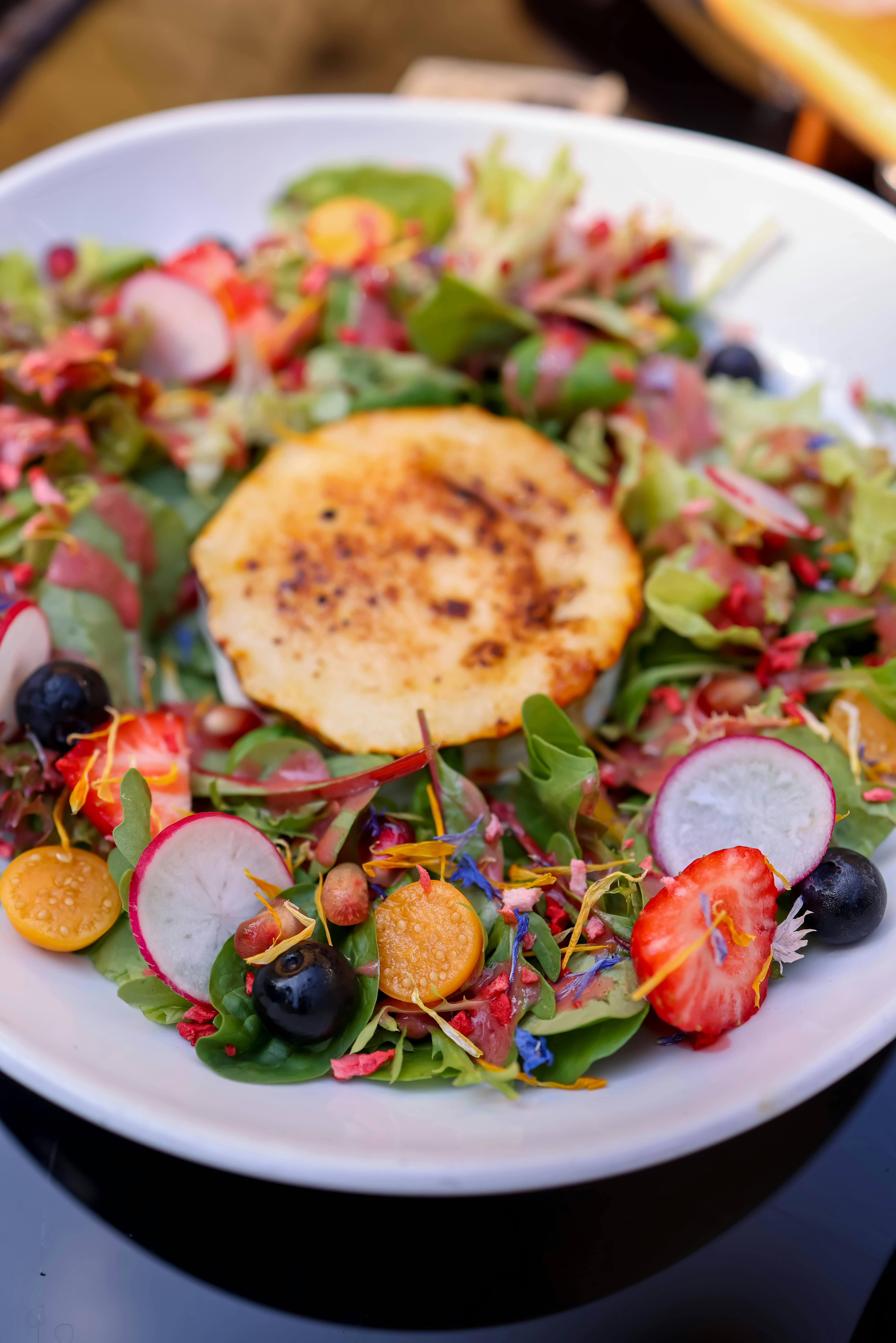 A fresh salad with grilled cheese, berries, and radishes on a white plate.