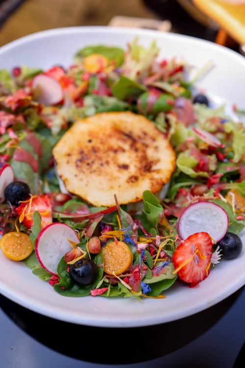 Free A fresh salad with grilled cheese, berries, and radishes on a white plate. Stock Photo