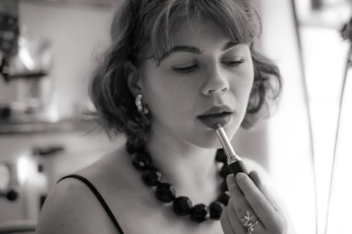 A woman in a black and white photo is applying lipstick