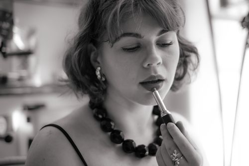 Free Black and white portrait of a woman applying lipstick, capturing elegance and glamour. Stock Photo