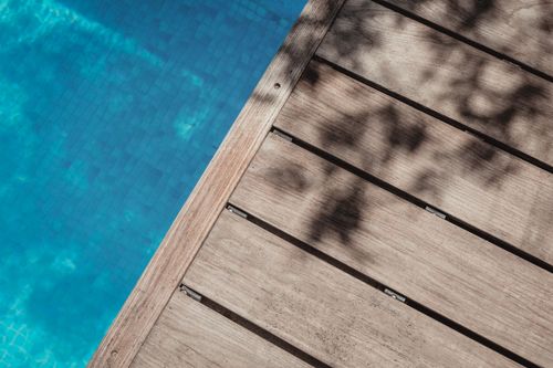 Free A wooden boardwalk casts shadows over a clear blue swimming pool, evoking a serene summer vibe. Stock Photo