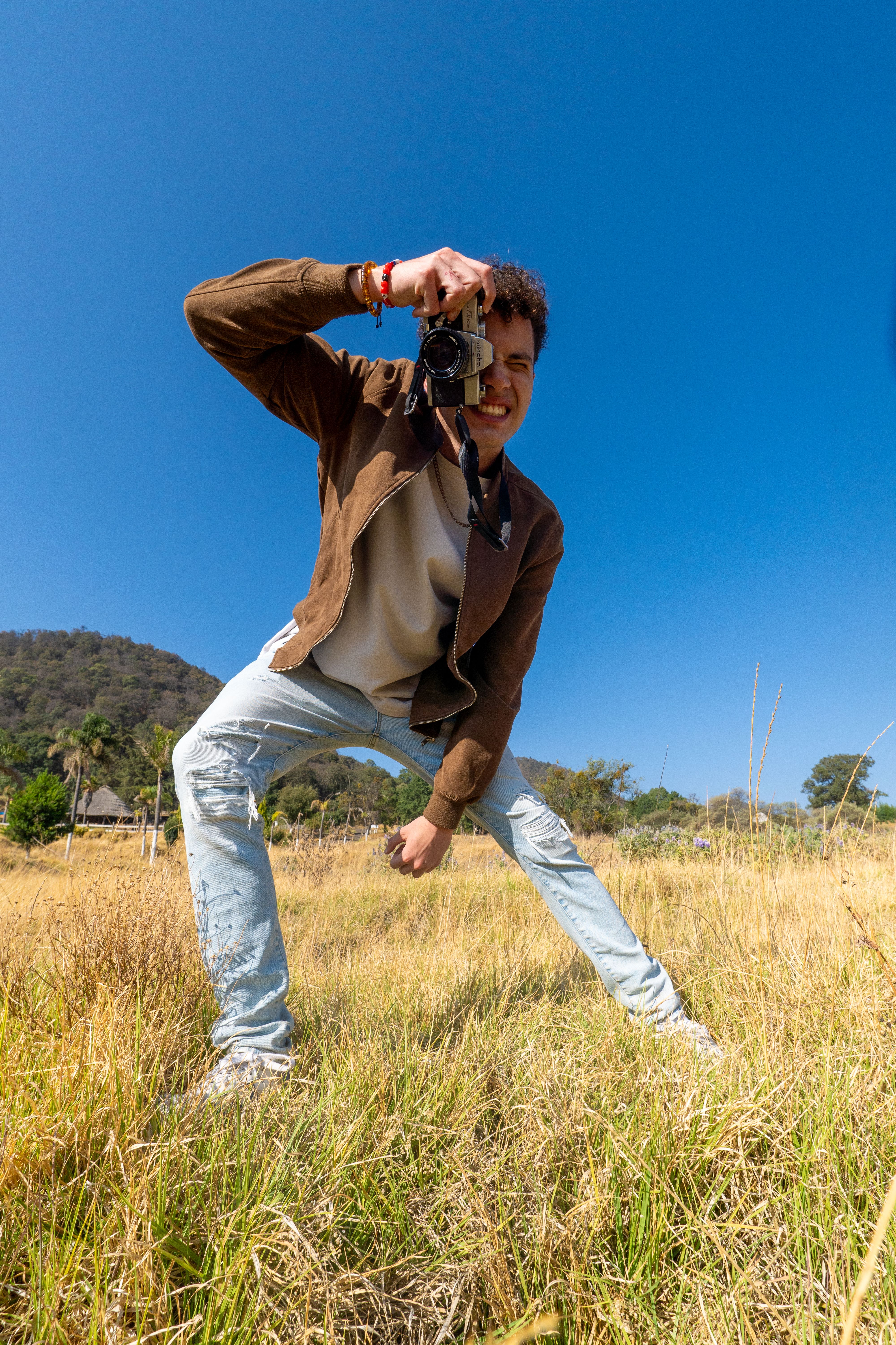 Young male photographer capturing dynamic shots in a sunny rural field in Amecameca, Mexico.