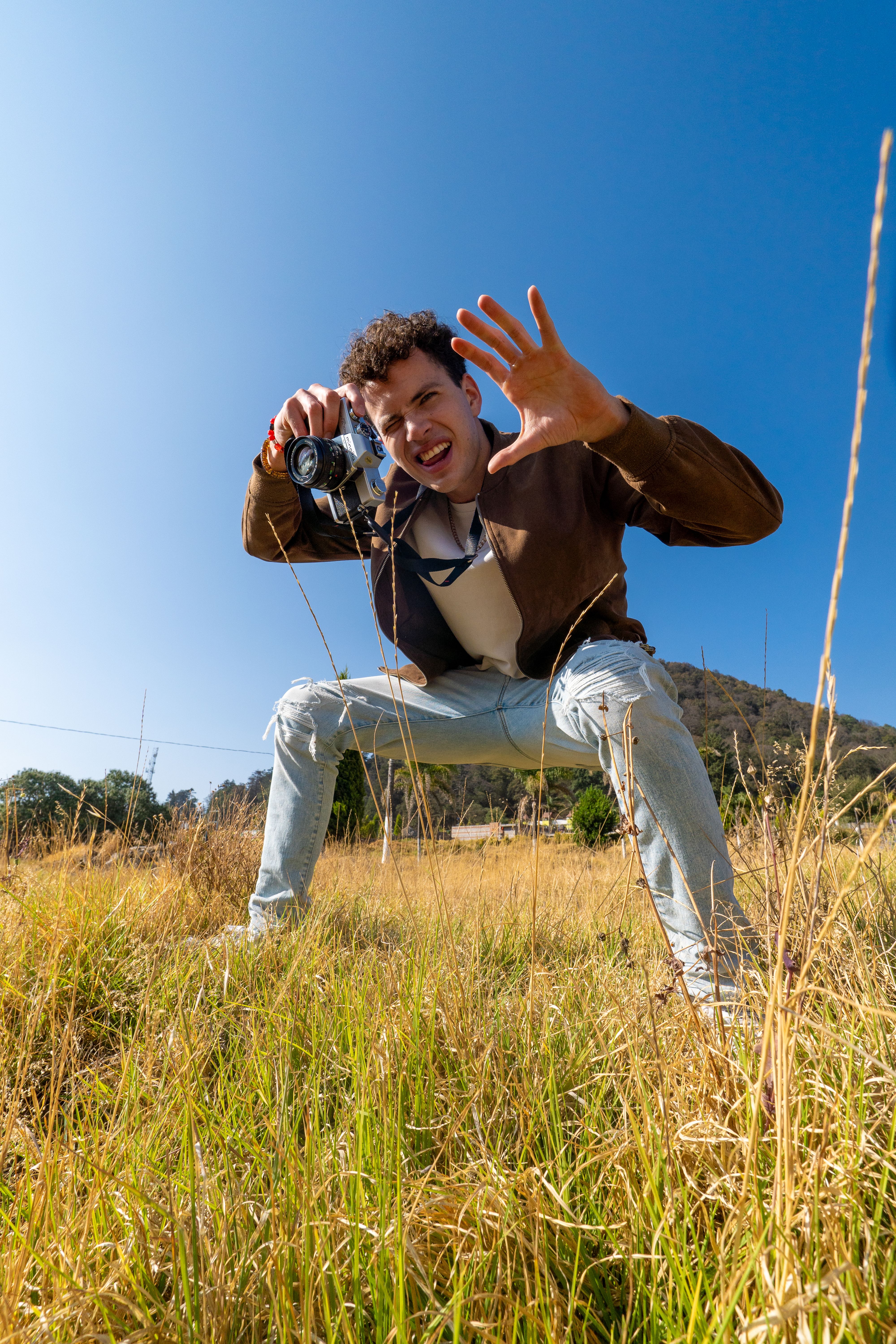Man enthusiastically posing with camera in a sunny Mexican field.