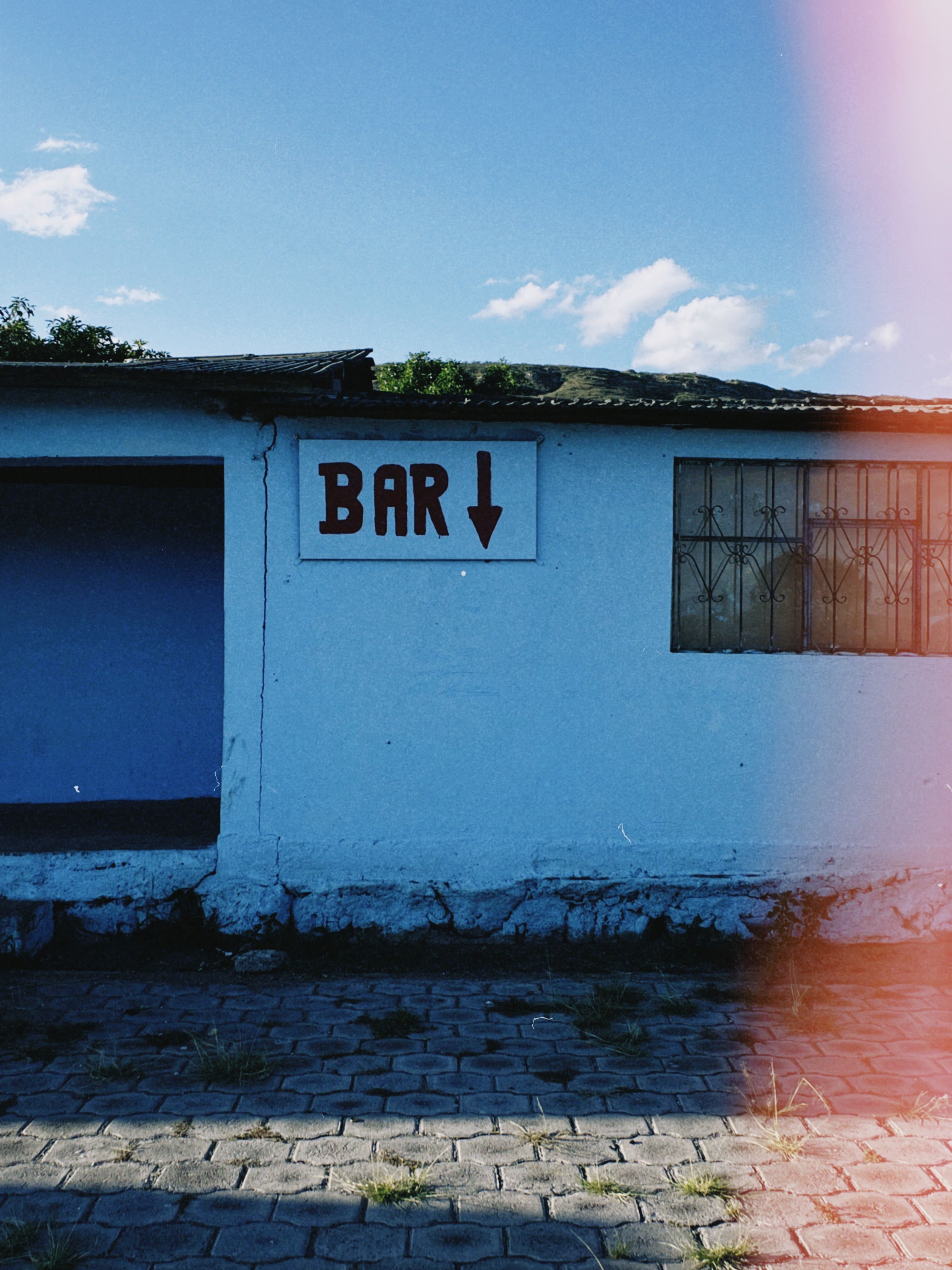 A quaint outdoor bar sign on a blue wall with urban street elements.
