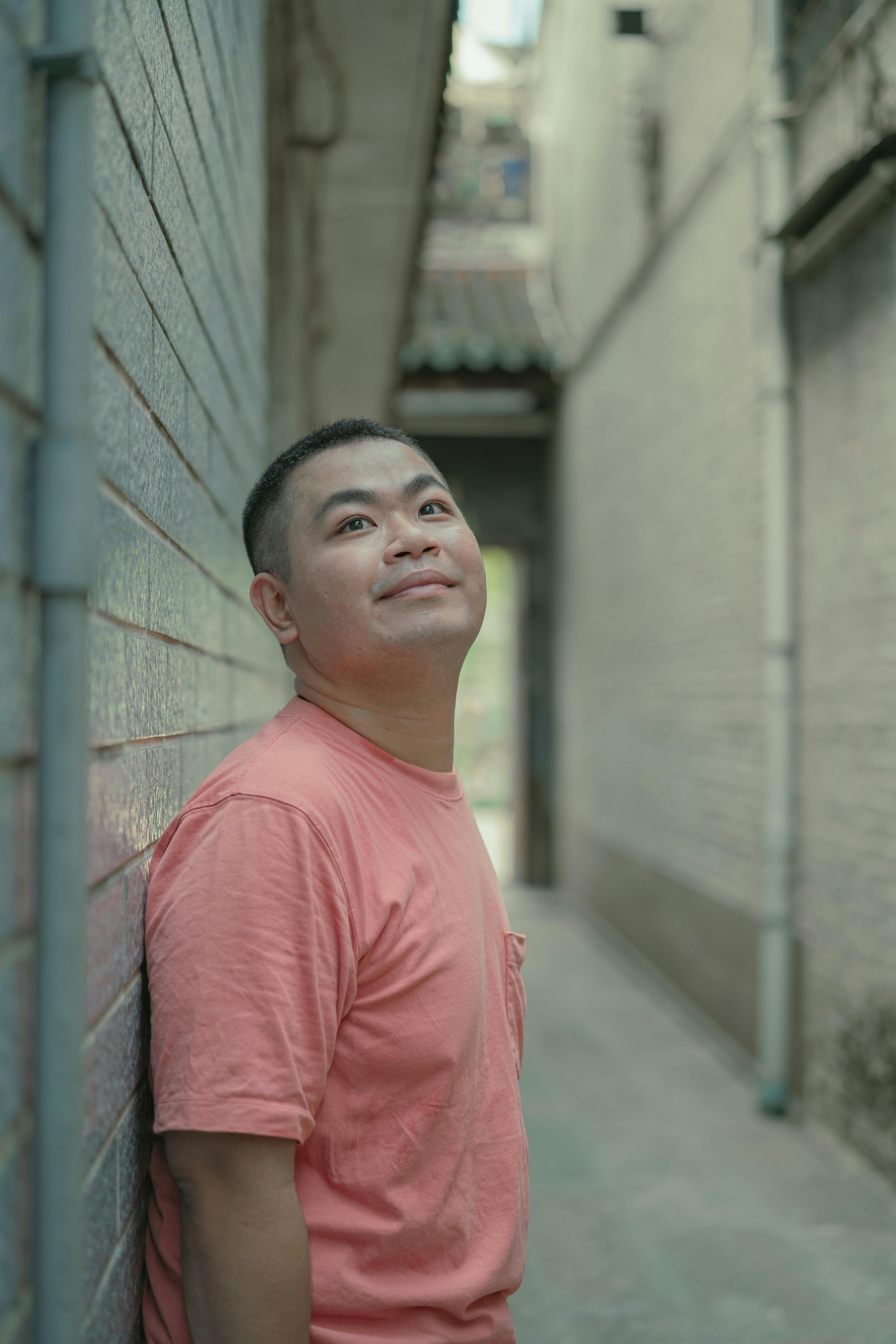 Portrait of a man in a pink t-shirt looking up in a narrow urban alley in Ho Chi Minh City.