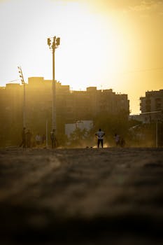 Silhouetted soccer players enjoy a game at sunset on an urban field.