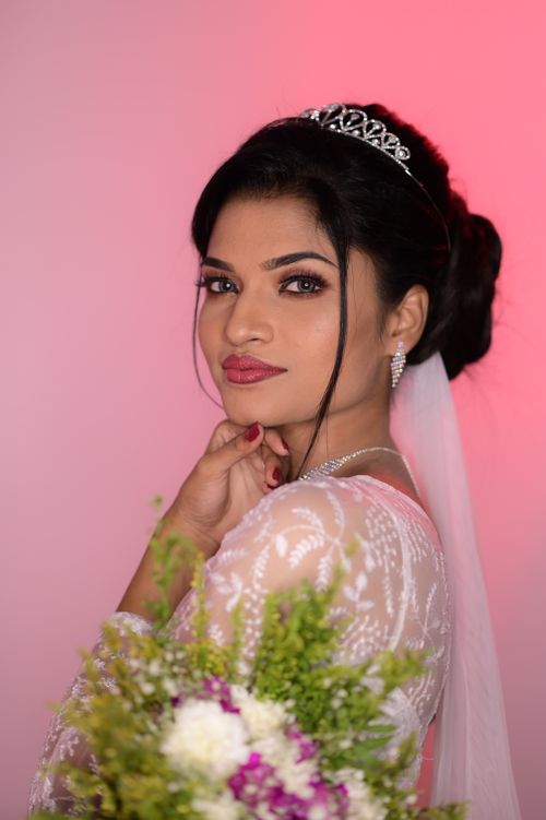 Free Portrait of a bride in a studio holding a bouquet, wearing a tiara and wedding dress on a pink background. Stock Photo