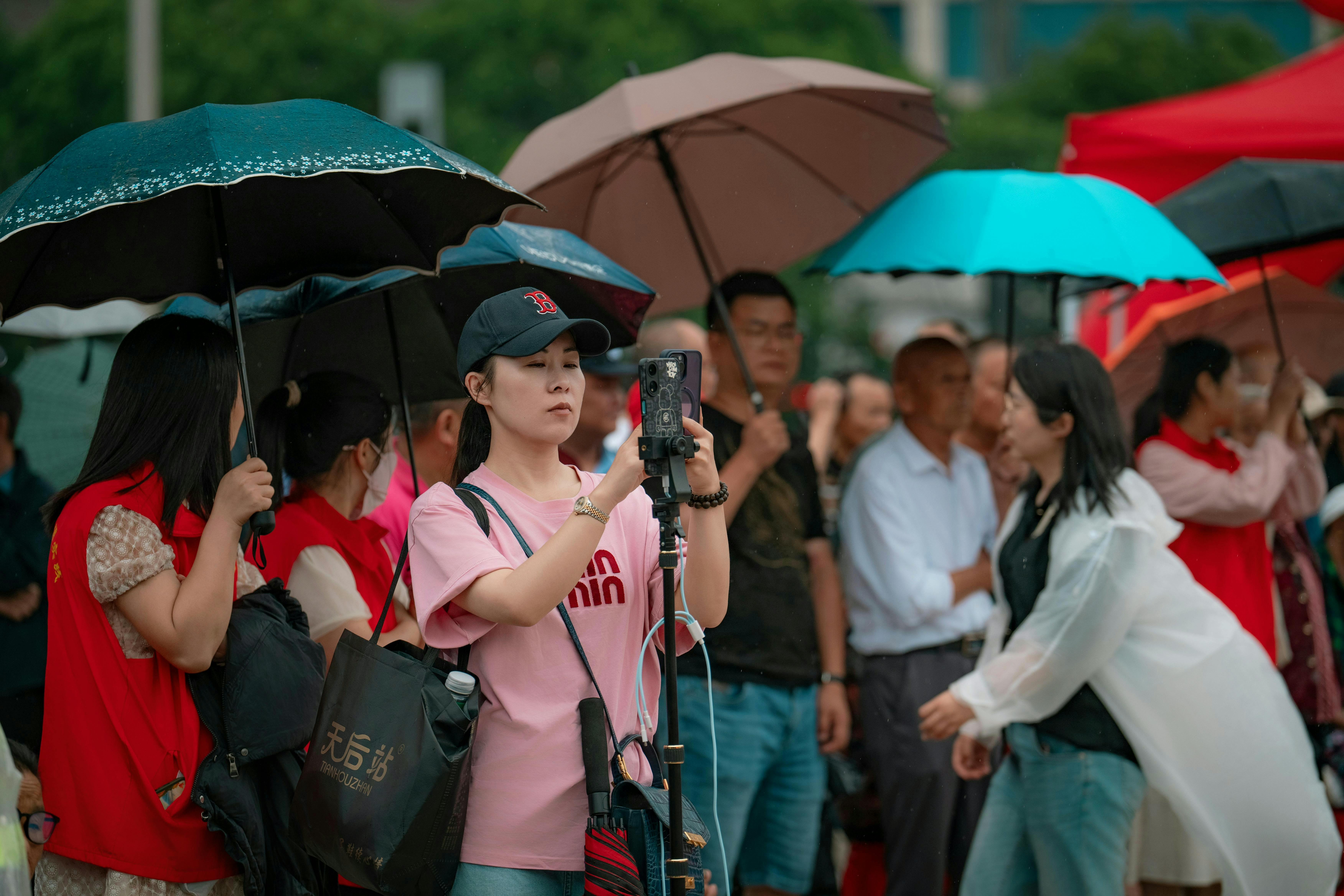A group of people using smartphones and umbrellas during a rainy event.