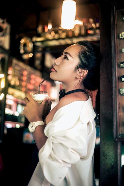 Free A woman enjoys a drink in a relaxed bar atmosphere, creating a casual and warm ambiance. Stock Photo